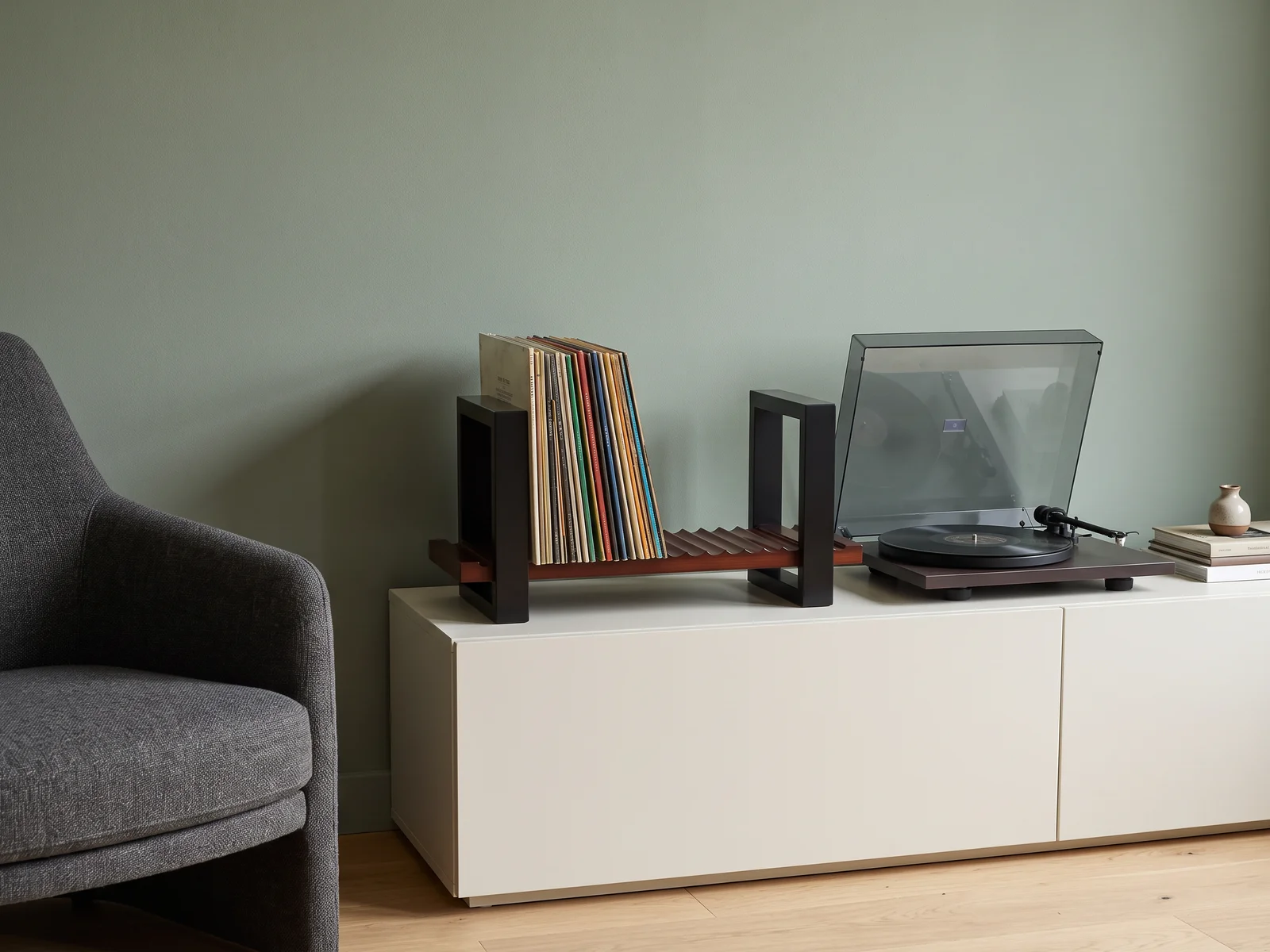 Illustrative vinyl record holder and turntable on a white cabinet against a sage wall