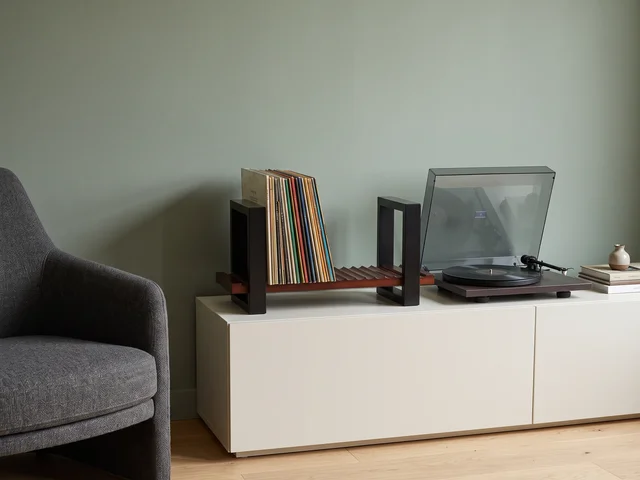 Illustrative wooden record holder with black brackets beside a turntable