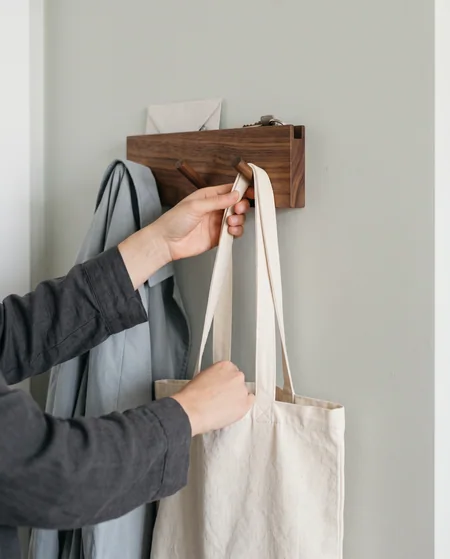 A hand hanging a bag on a wall organizer in a bright home